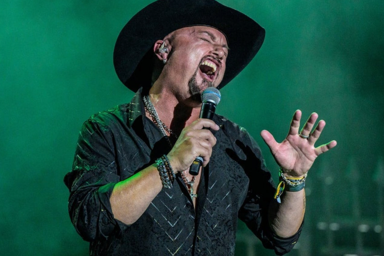 Live performance portrait of former Queensrÿche singer Geoff Tate wearing a black cowboy hat and passionately singing into a microphone on stage.